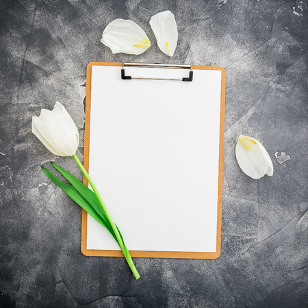 Composition with clipboard and white tulips on dark background. Flat lay, top view. Floral background.の写真素材