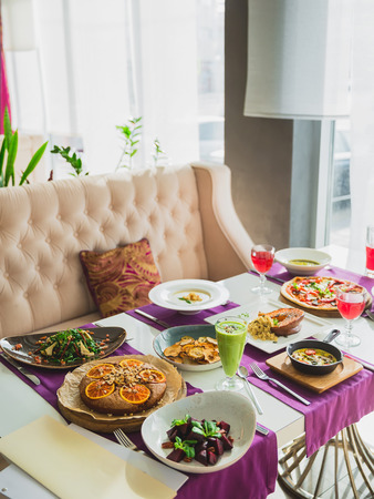 Table in cafe with vegetarian dishes - pizza with vegetables, salads, pie and fresh natural drinks.の写真素材