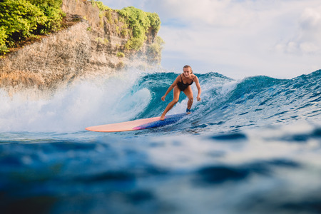 Surfer woman at surfboard ride on ocean wave. Woman in ocean during surfing.