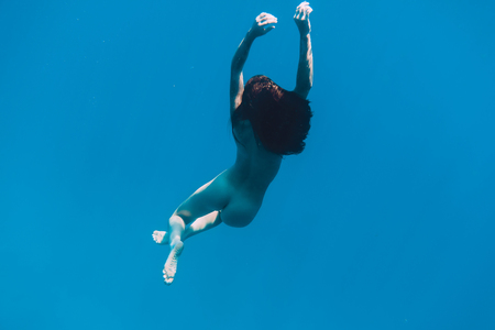 Young woman in underwater. Beautiful woman with naked body in blue seaの写真素材