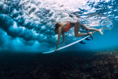 Professional surfer woman with surfboard make up duck underwater with ocean wave.