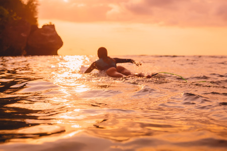 Surfer girl on a surfboard Surfing at sunsetの写真素材
