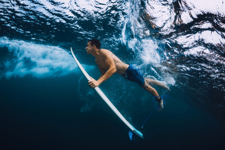 Surfer man with surfboard dive underwater with ocean wave.