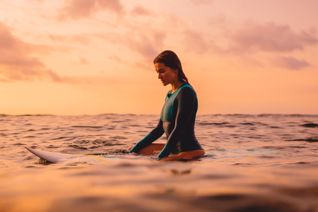 Surfer woman with perfect body on a surfboard in ocean. Surfing at sunset