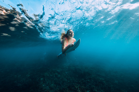 Attractive surfer woman in bikini with surfboard dive underwater with under barrel waveの写真素材