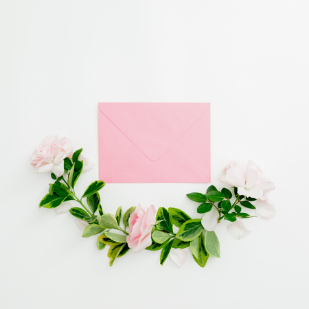 Floral composition of paper envelope with pastel pink roses and green leaves on white background. Flat lay, top view. Spring time.の写真素材