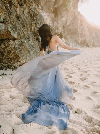 Brunette woman posing in stylish blue dress at beach. Fashion woman.の写真素材