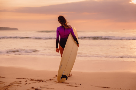 Surf girl with surfboard on a beach at sunset or sunrise.の写真素材