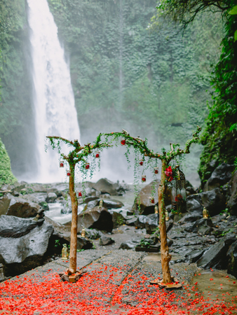 Arch with beautiful flowers and red petals. Wedding ceremony at waterfall.の写真素材