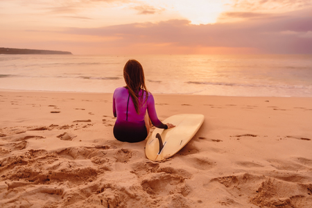 Surf girl with surfboard relax on a beach at sunset or sunrise. Surfing at sunsetの写真素材