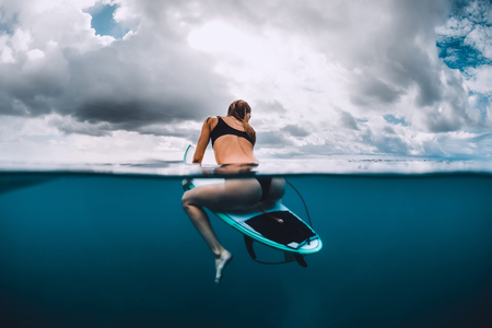 Surf girl sit at surfboard in blue oceanの写真素材
