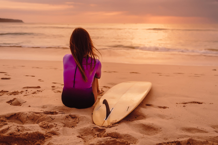 Surfer woman with surfboard relax on the beach at sunset or sunrise.の写真素材