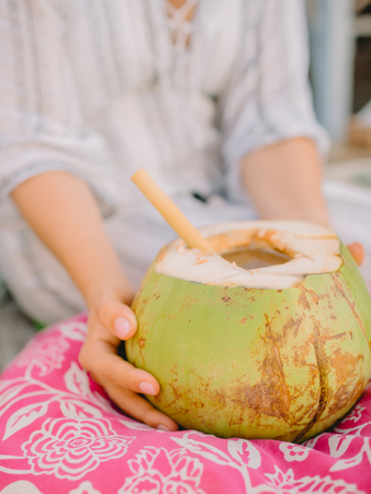 Woman hands and fresh coconut with bamboo straw on tableの写真素材