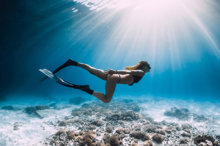 Pretty woman freediver with fins swim over sandy sea and sun rays underwaterの写真素材