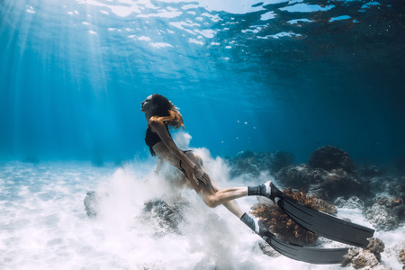 Woman freediver with fins swim over sandy bottom and sun rays underwater oceanの写真素材