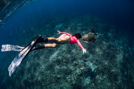 Young woman freediver with fins swim underwater with sea turtle.の写真素材