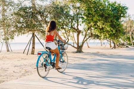 Happy young woman on blue bicycle near ocean in tropical islandの写真素材