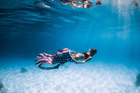 Woman freediver glides over sandy sea bottom with United States flag. Independence day.の写真素材