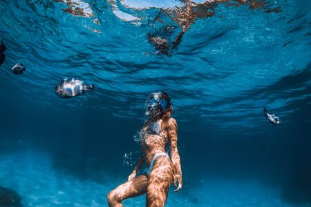 Freediver girl with with fishes in transparent ocean