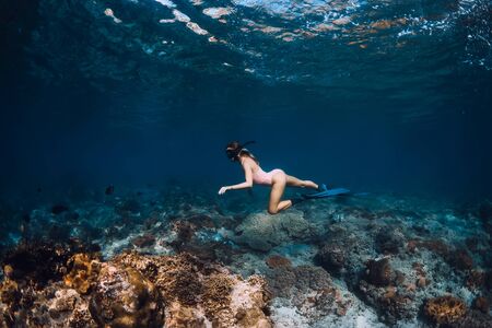 Slim woman freediver glides over bottom with fish in underwaterの写真素材