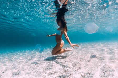 Woman underwater posing with jellyfish. Swimming in blue ocean with sand