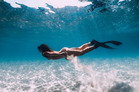 Freediver girl with fins glides over sandy sea in transparent ocean.の写真素材