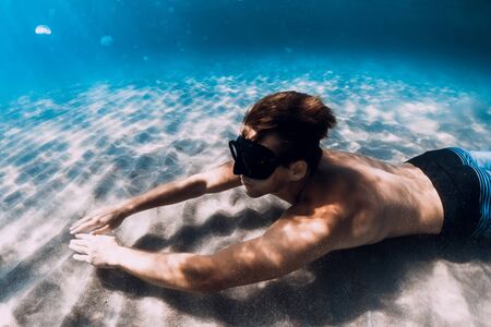 Freediver glides underwater over sandy bottom. Swimming underwater with finsの写真素材
