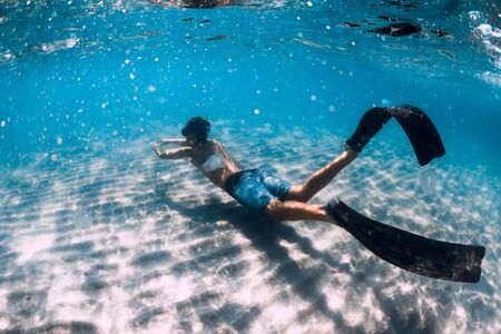 Freediver glides underwater over sandy bottom. Swimming underwater with finsの写真素材