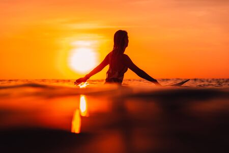 Attractive surfer woman on a surfboard in ocean. Surfgirl at sunsetの写真素材