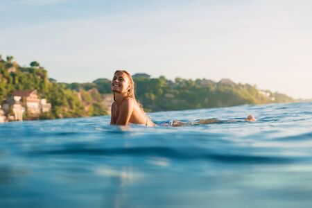 Attractive surfer girl on a surfboard in ocean.