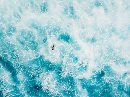 Aerial view of surfer and blue foamy ocean. Top view