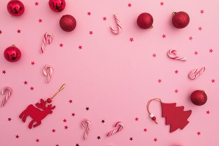 Christmas or New Year frame composition. Red toys, candy canes and confetti on pink. Flat lay, top view.の写真素材