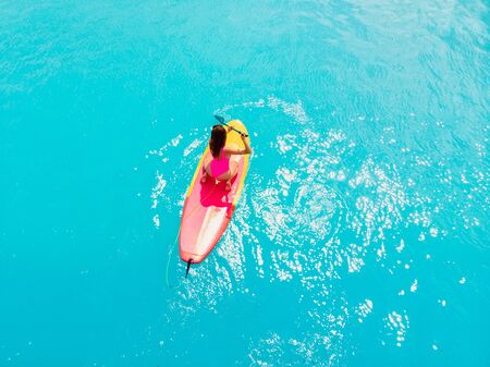 Attractive woman in swimwear floating on stand up paddle board on a quiet blue ocean.