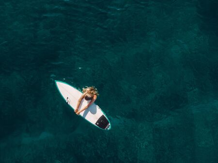 March 02, 2019. Bali, Indonesia. Aerial view of attractive surfer woman relax with surfboard in tropical ocean.のeditorial素材