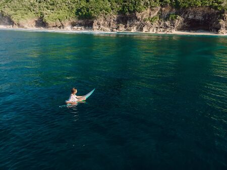 March 02, 2019. Bali, Indonesia. Aerial view of attractive surfer woman relax with surfboard in tropical ocean.のeditorial素材