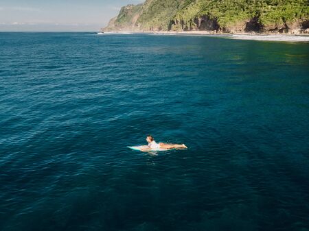 March 02, 2019. Bali, Indonesia. Aerial view of attractive surfer woman relax with surfboard in tropical ocean.のeditorial素材