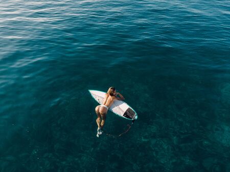 March 02, 2019. Bali, Indonesia. Aerial view of attractive surfer woman relax with surfboard in...