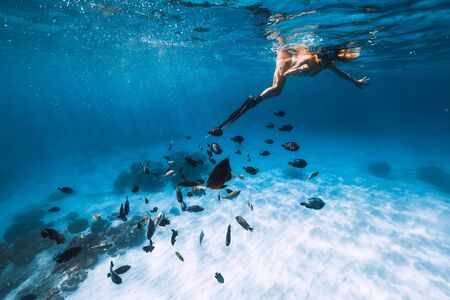 Young woman freediver in bikini snorkeling over sandy sea with fishes.