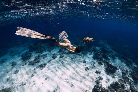Free diver with fins glides underwater with turtle in ocean. Snorkeling with sea turtle.の写真素材