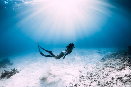 Freediver girl with fins glides over sandy sea in ocean. Freediver and amazing light