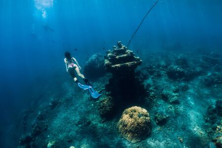 Young woman free diver glides with fins near underwater temple. Freediving in blue ocean