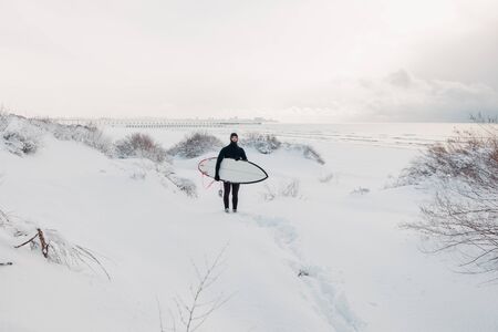 Cold winter and surfer with surfboard. Snowy day with surfer in wetsuit.の写真素材