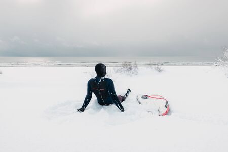 Cold winter and male surfer relax on snow with surfboard. Snowy day with surfer in wetsuit.の写真素材