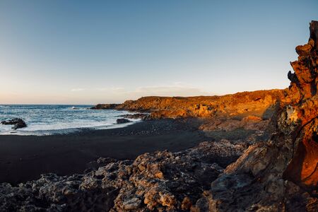 Beach with lava cliffs and ocean at sunset in Lanzarote, Canary Islands.