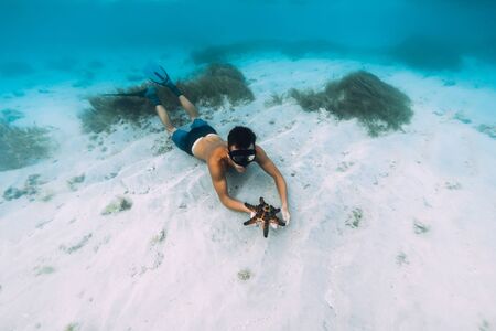 Freediver man with hold starfish and relax over sandy bottom in blue oceanの写真素材