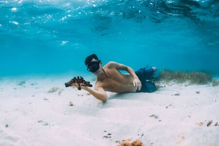 Freediver man with hold starfish and relax over sandy bottom in blue oceanの写真素材
