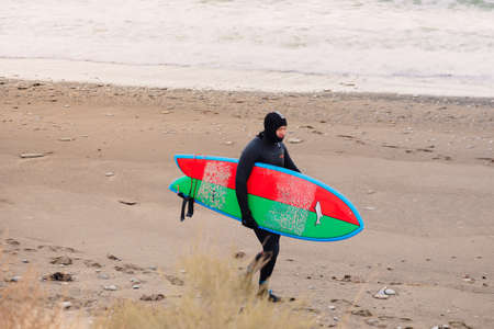 November 22, 2019. Crimea, Russia. Surfer in wetsuit with surfboard at beach.