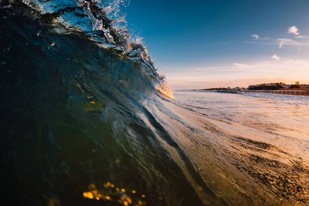 Barrel wave in ocean with sunrise tones and beach at backgroundの写真素材
