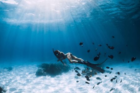 Free diver young woman with fins glides over sandy bottom with tropical fishes in transparent oceanの写真素材