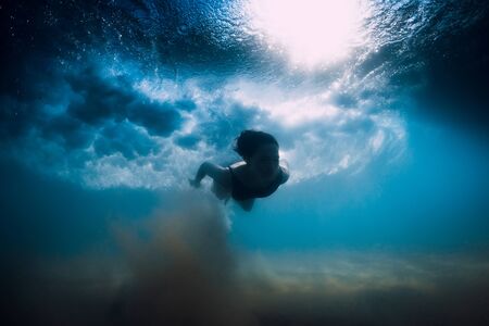 Woman dive without surfboard under ocean wave. Underwater duck dive under wave and sandy bottom